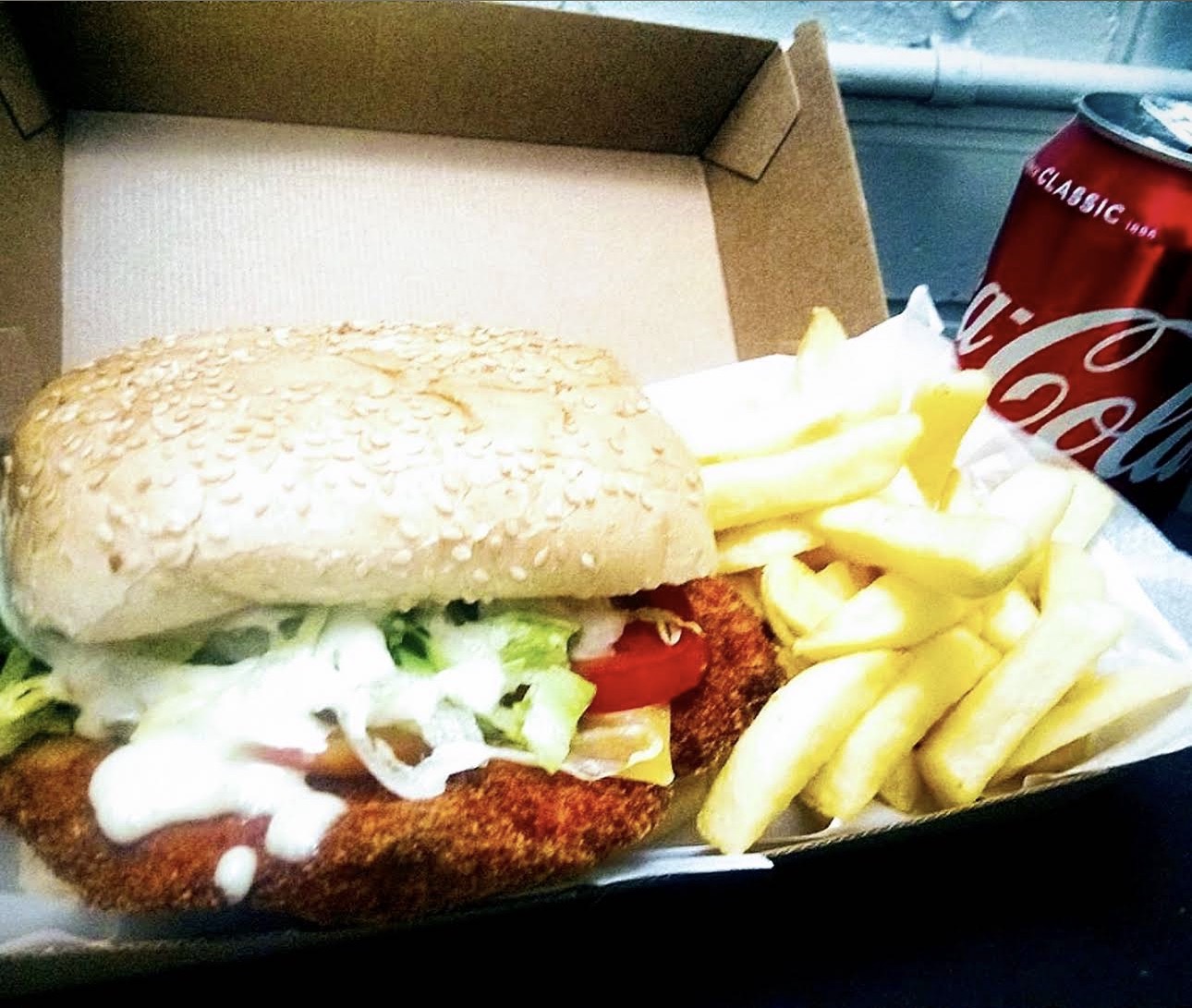 Chicken schnitzel roll with salad and chips in a takeaway box with a Coke